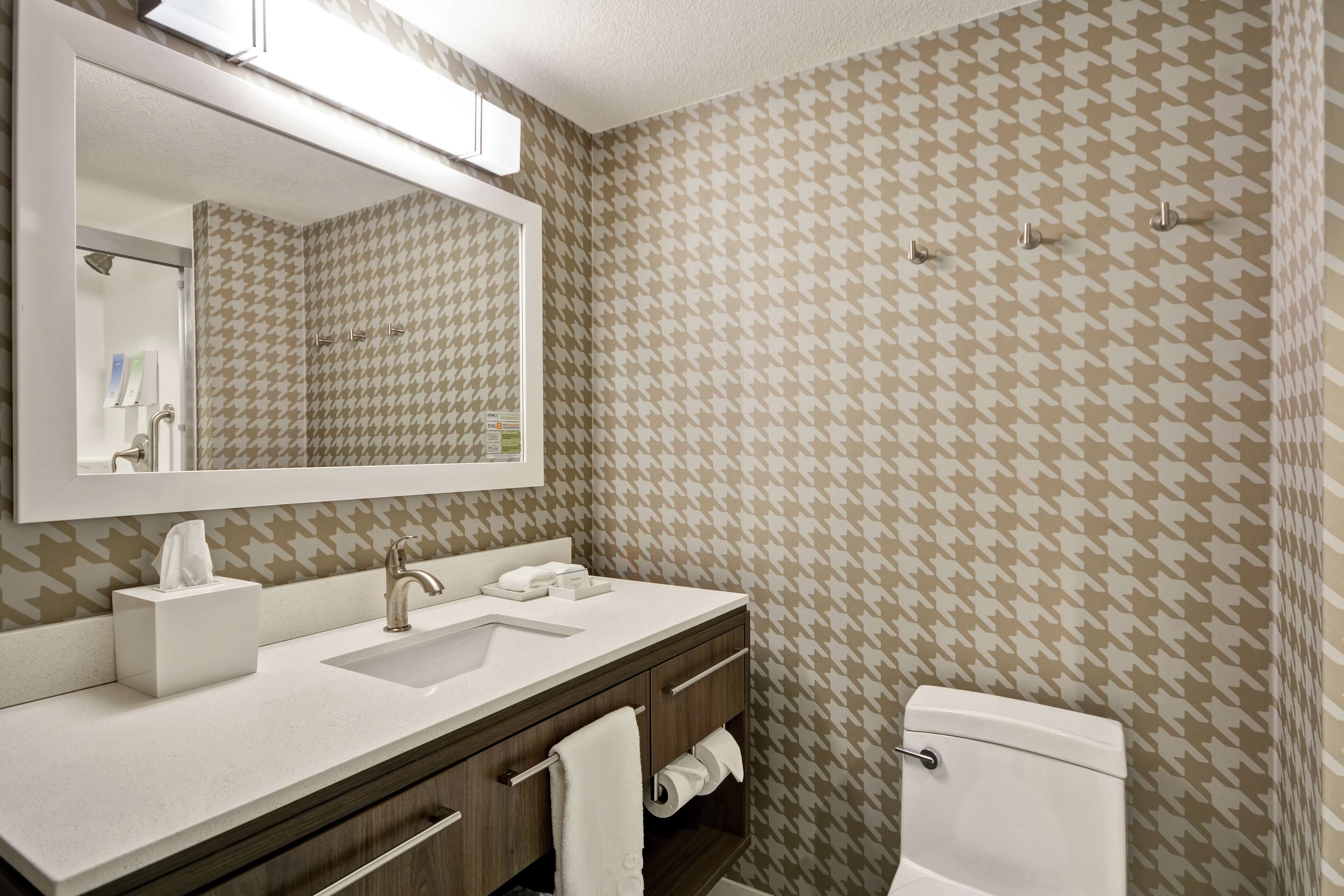 A bathroom with a houndstooth patterned wall, a white sink, a mirror, and a toilet.