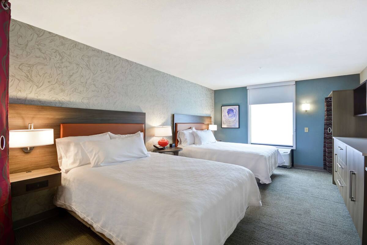 Ett hotellrum med två sängar, ett skrivbord, en lampa, en tv och ett fönster.