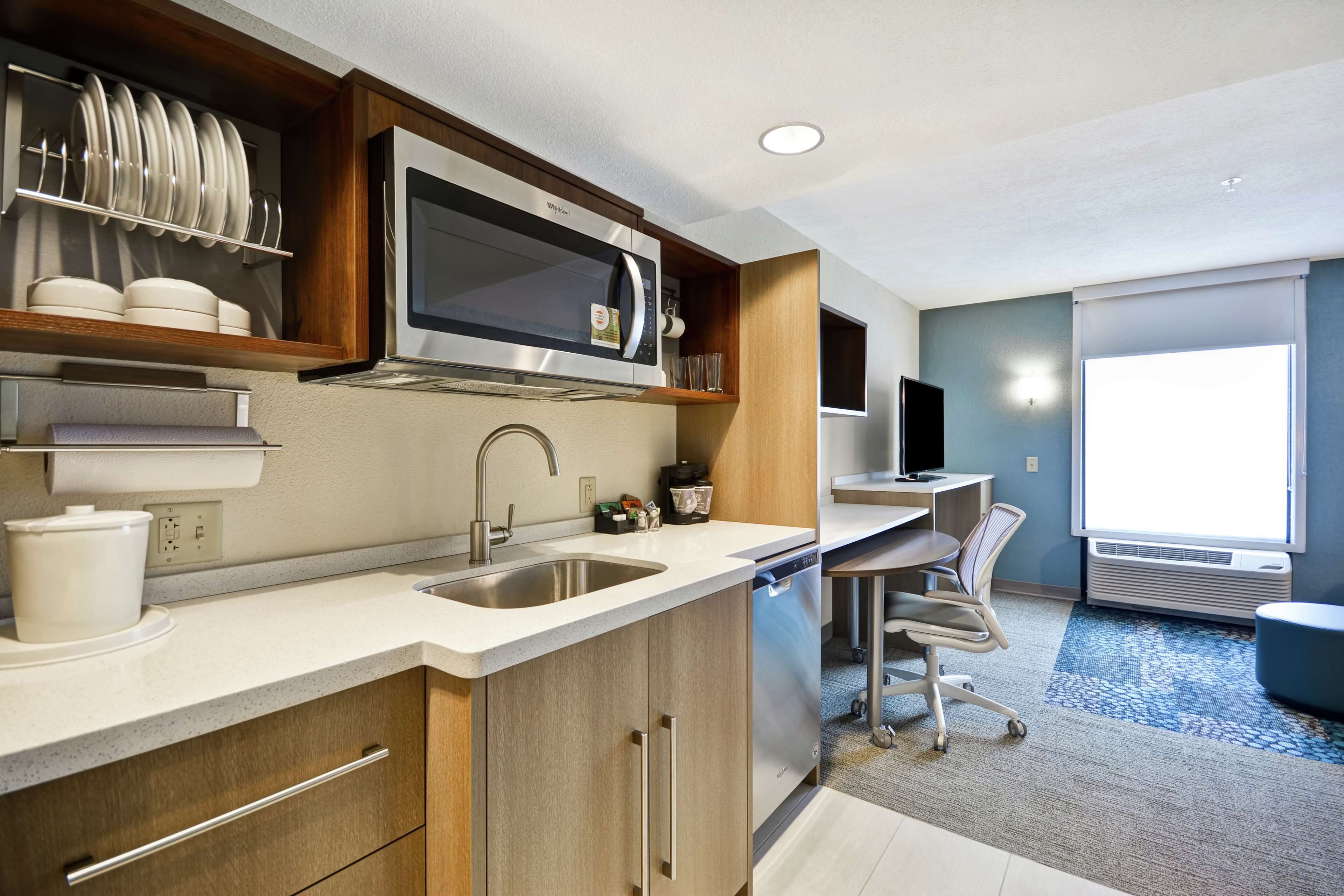 A compact kitchen with a microwave, sink, and dish rack. There is a small seating area with a chair and a table.