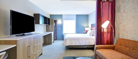 Hotelkamer met flatscreen televisie, een bed, een sofa, bureau en raam met gordijnen.