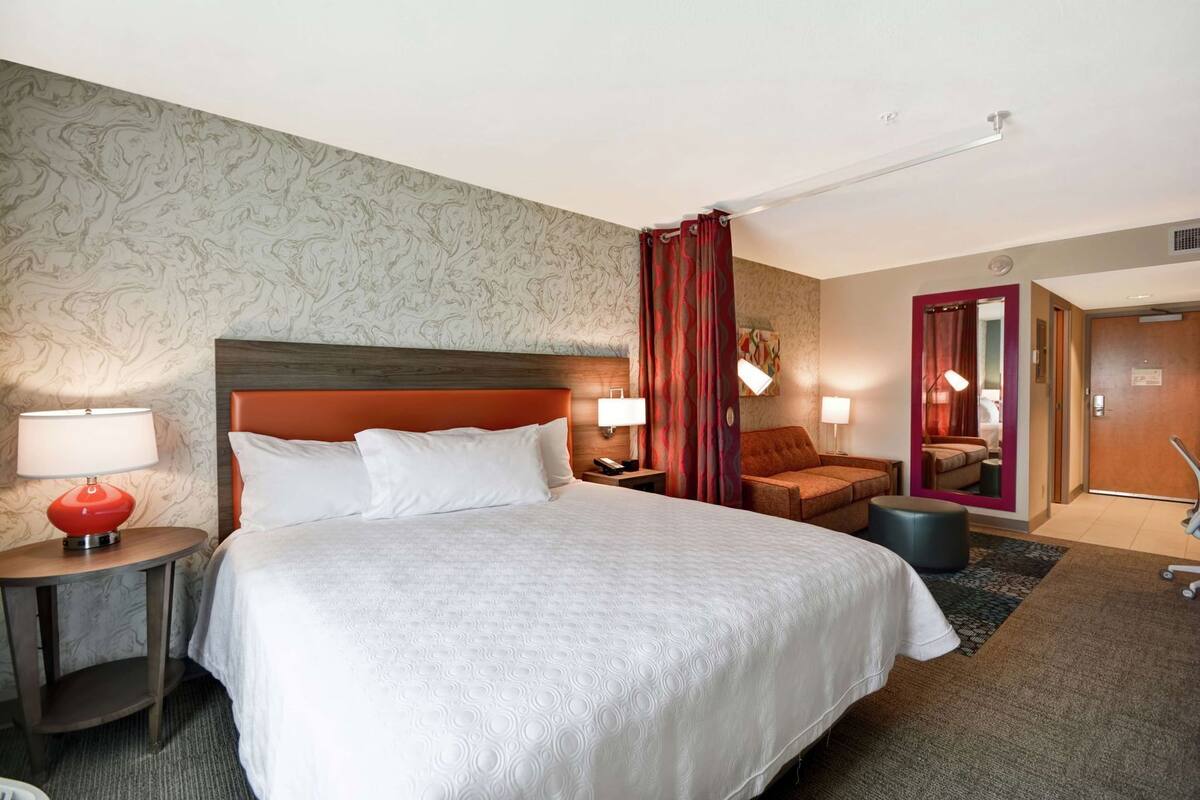 Ett hotellrum med en stor säng, två sängbord med lampor, en soffa, en spegel och en dörr som leder till ett annat rum.