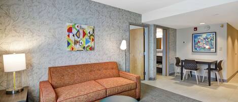 Ein Hotelzimmer mit einer Couch, Hocker und einem Essbereich mit Stühlen und einem Tisch.