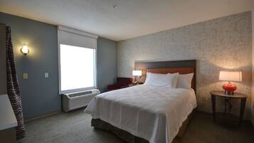 A hotel room with a large bed, a window with blinds, a red chair, a nightstand with a lamp, and a wall with a marble-like pattern.