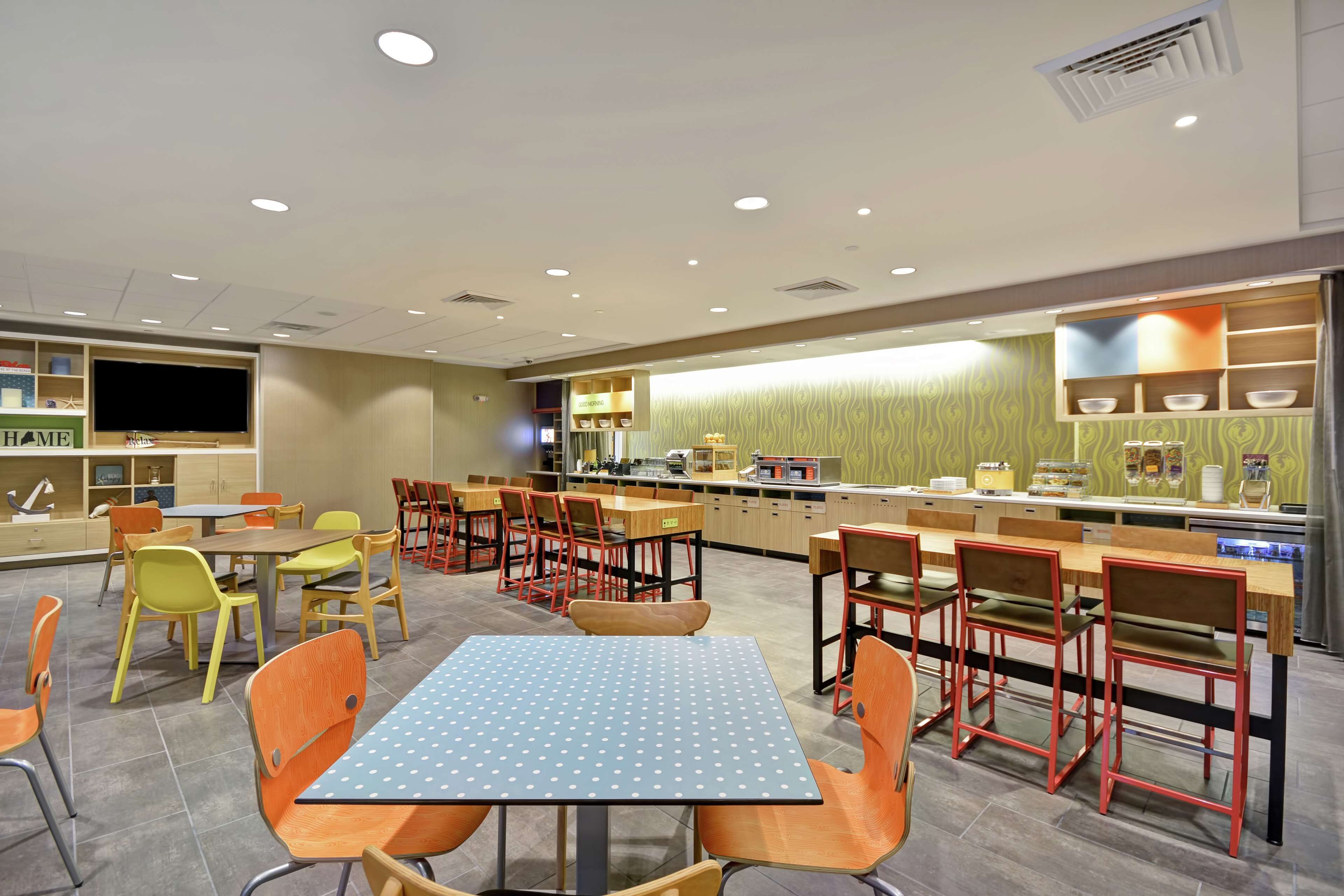 Un espace repas moderne avec plusieurs tables et chaises, un comptoir de cuisine et un téléviseur.