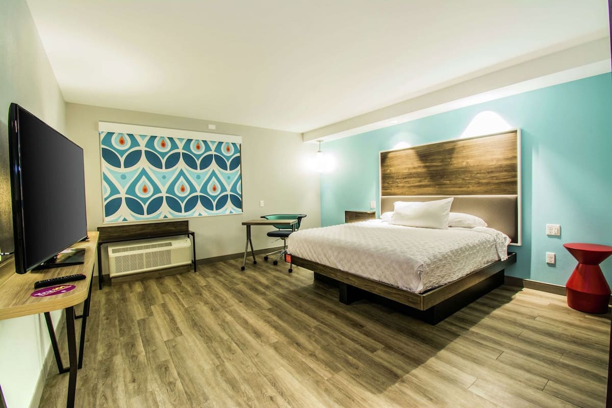 A hotel room with a bed, a desk, a TV, and a wall with a geometric pattern.