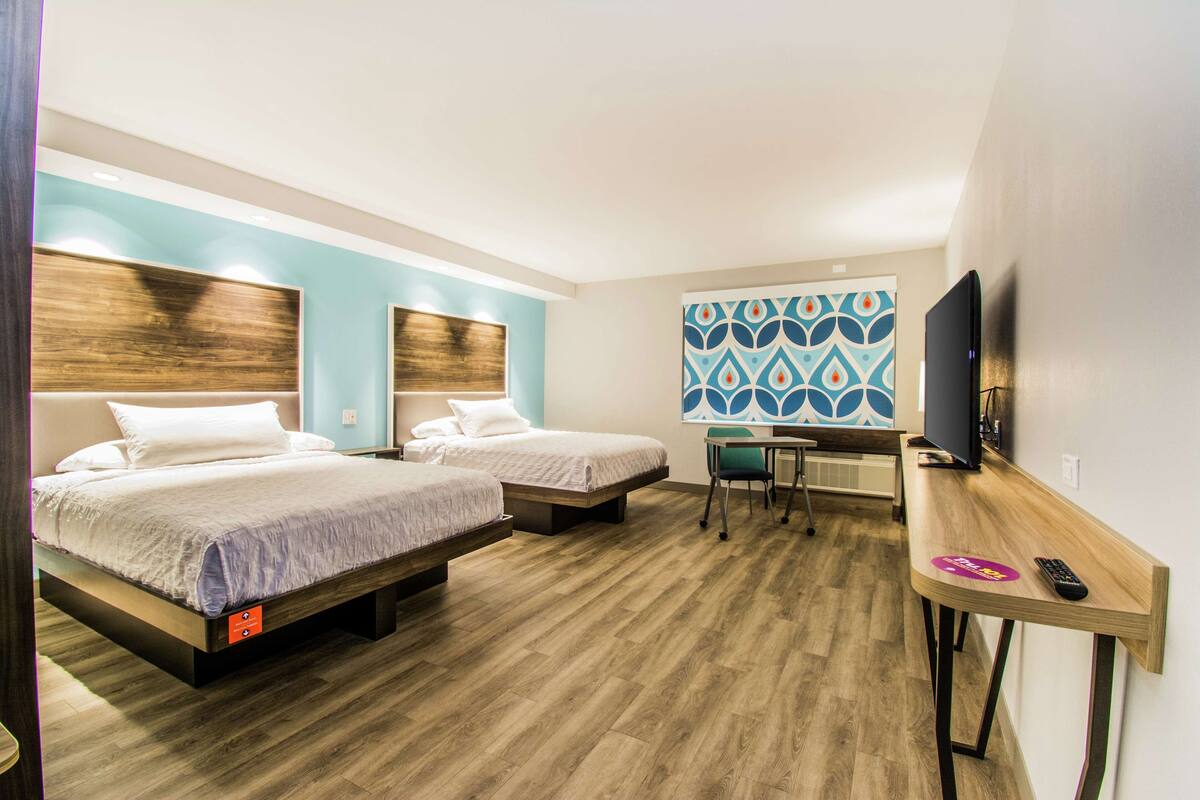 A hotel room with two beds, a desk with a chair, a television, and a patterned wall.
