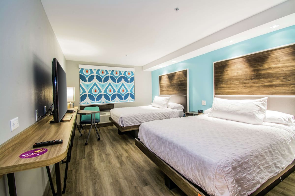 A hotel room with two beds, a desk with a TV, and a patterned wall.