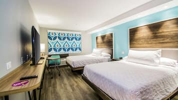 Habitación de hotel con dos camas, un escritorio y un televisor, y una pared con diseño.