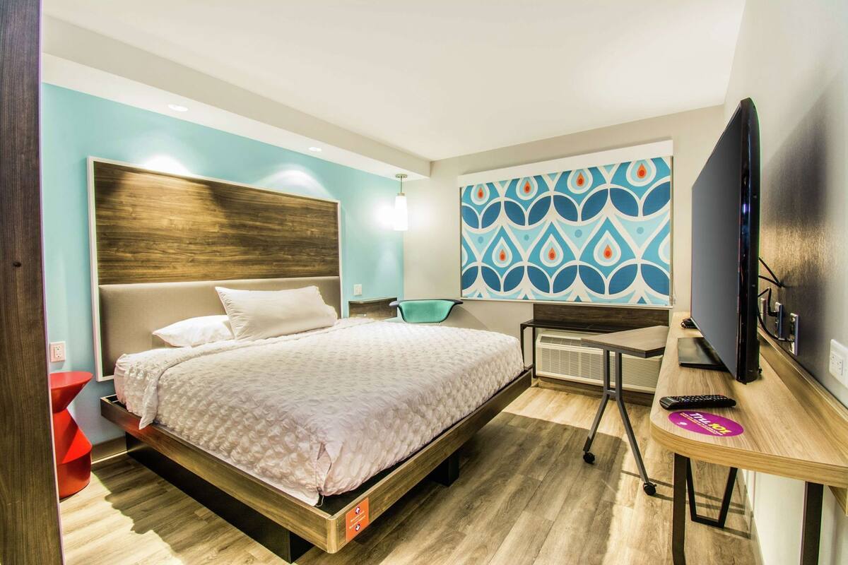 A modern hotel room with a bed, a desk, a television, and a patterned wall.