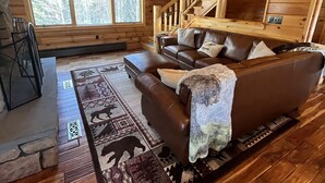 Ein rustikales Holzhaus-Interieur mit einer braunen Ledersofa, einem gemusterten Teppich und einer Holztreppe.