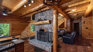Ein Blockhaus-Interieur mit Kamin aus Stein, Holzdielen, einer Küche mit Granit-Arbeitsplatten und einer gemütlichen Sitzecke.