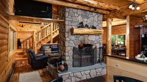 Ein gemütliches Blockhaus-Interieur mit Kamin aus Stein, Ledersitzmöbeln, einem Essbereich und einer Küche.