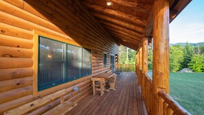 Eine Blockhütte mit einer Holzdachterrasse, großen Fenstern und Blick auf einen bewaldeten Bereich.