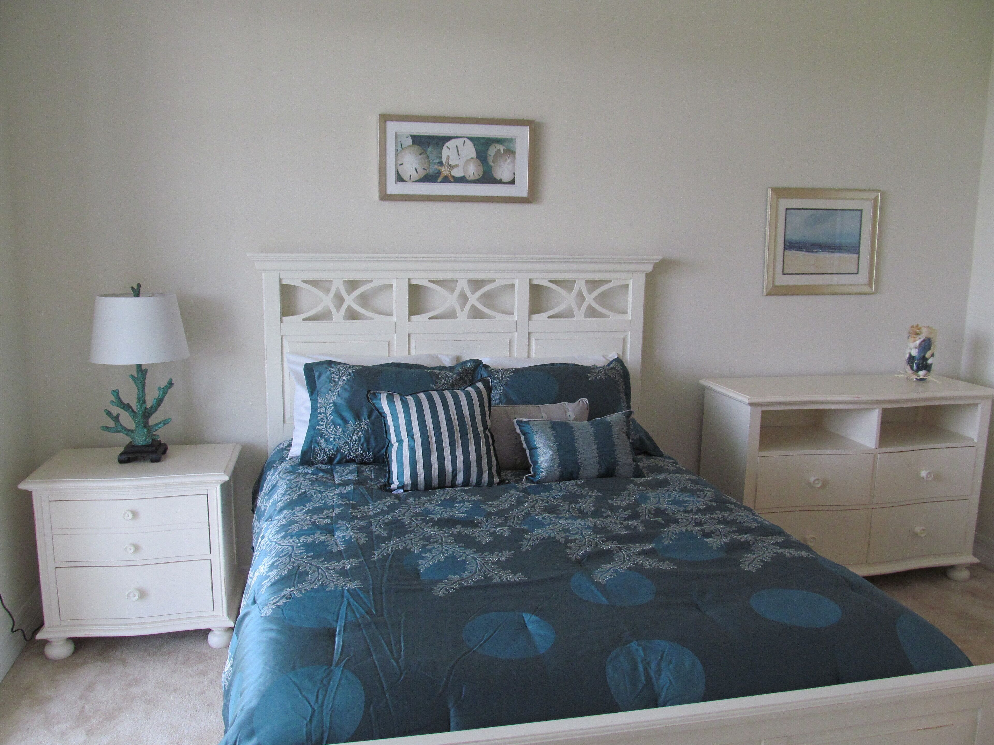 A bedroom with a bed, nightstands, a dresser, and wall art.