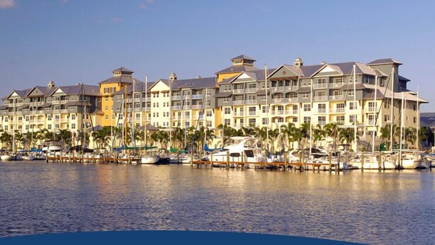Un hotel frente al agua con varios balcones, un puerto deportivo con barcos y palmeras.