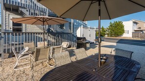 Un espace extérieur aménagé avec une table et des chaises, un barbecue et un grand parasol pour faire de l’ombre.