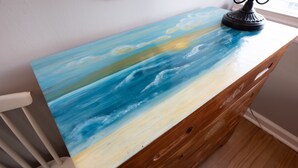 Une commode en bois sur laquelle est peinte une scène marine.