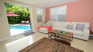 A living room with a white sofa, a wooden coffee table, and a dining table. There is a pool visible through the glass door. - BY THE SEA VACATION VILLAS 4 BED/PRIVATE POOL/ WALK TO EVERYTHING. Amazing location! (Lauderdale-by-the-Sea)