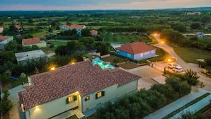 A residential area with houses, a swimming pool, and a well-lit street at dusk. - Great Villa Field Hills with sauna and jacuzzi (Poljica-Brig)