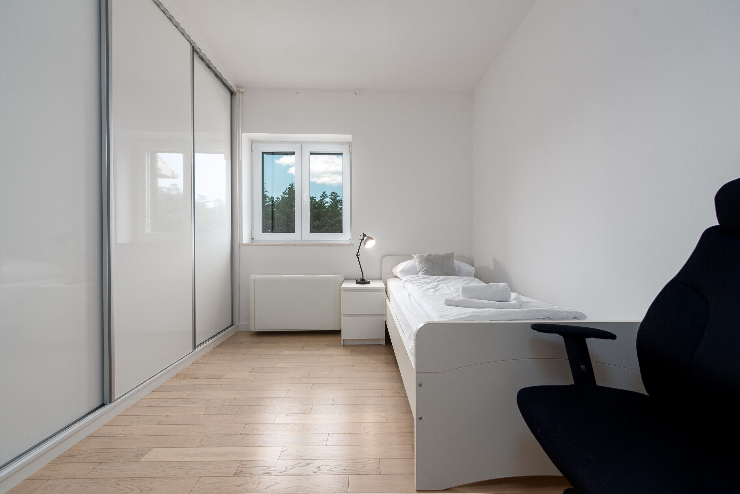 Un dormitorio con cama, mesita de noche, lámpara y ventana.