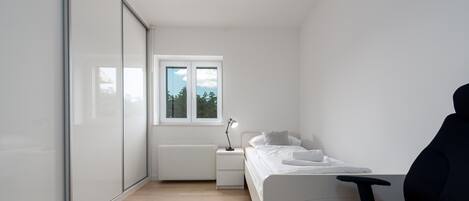 Un dormitorio con cama, mesita de noche, lámpara y ventana.