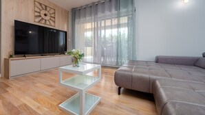 A modern living room with a flat-screen TV, a glass coffee table, a grey sofa, and a large window with sheer curtains. - Great Villa Field Hills with sauna and jacuzzi (Poljica-Brig)