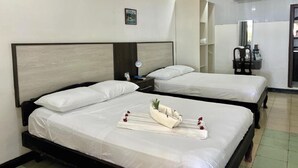 Et hotelværelse med to senge, et natbord med lampe, et spejl og en lille hylde med toiletartikler.