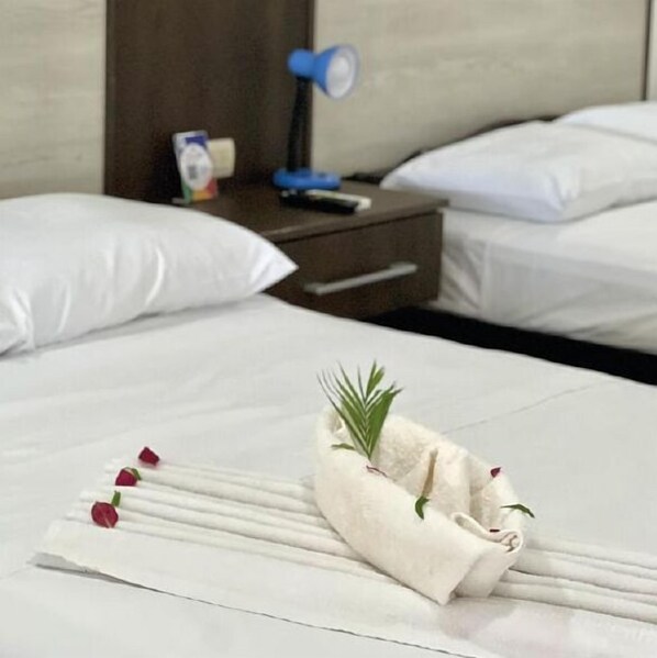 A neatly made bed with white linens, a folded towel with a sprig of greenery, and a few rose petals on the bed. - Hotel Claudio & Gloria Beach Front (Sardinal)