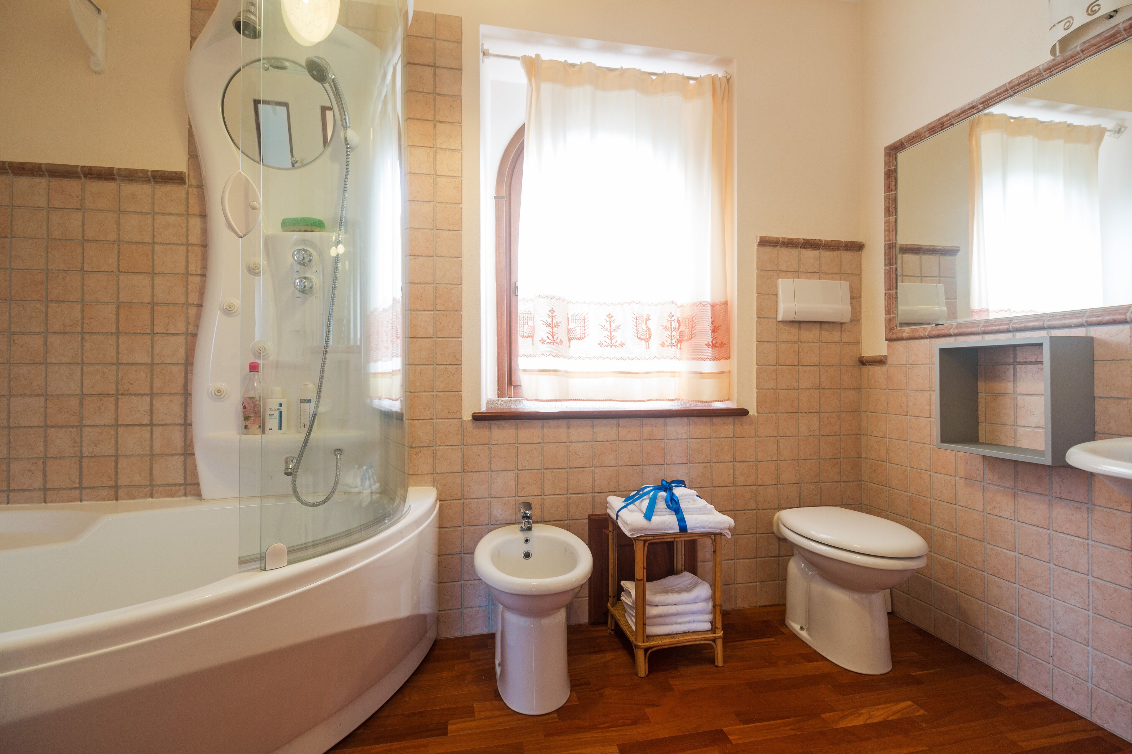 Et badeværelse med en glasafskærmet brusekabine, et væghængt håndvaskarrangement, et toilet og en kommode med spejl.