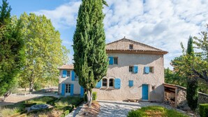 A two-story stone house with blue shutters, a stone pathway, and surrounding greenery. - Villa in Saignon with Pool and Scenic Views (Saignon)