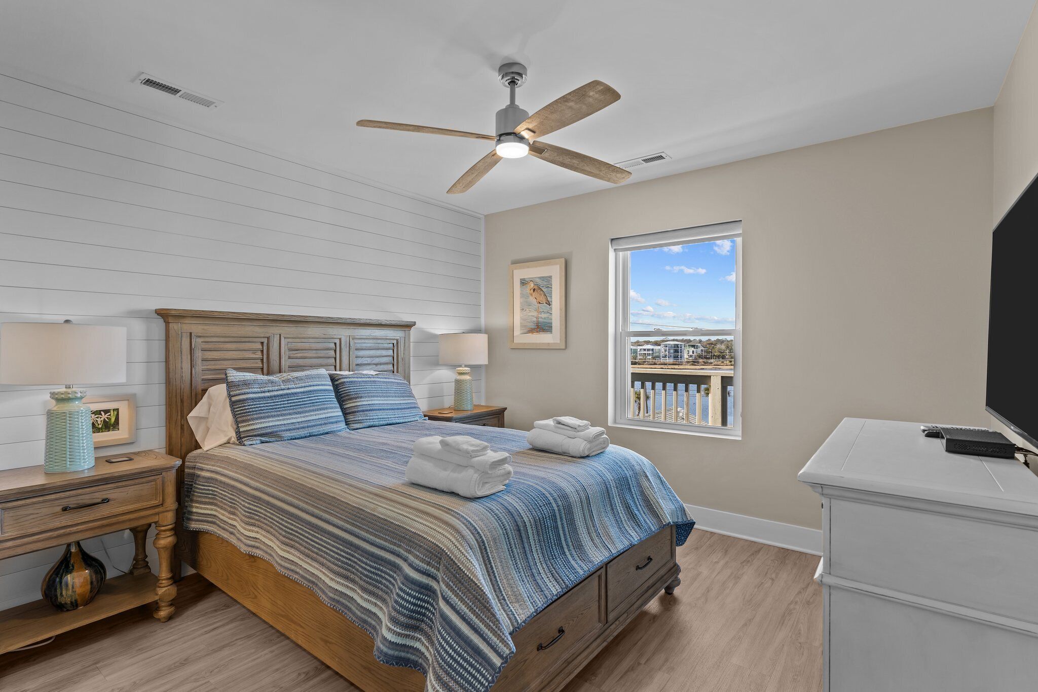 A bedroom with a bed, nightstands, a ceiling fan, a window with a view, and a TV on a stand.