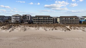 Een strandhotel met meerdere gebouwen, waaronder een opvallend gebouw met een balkon en een trap naar het strand.