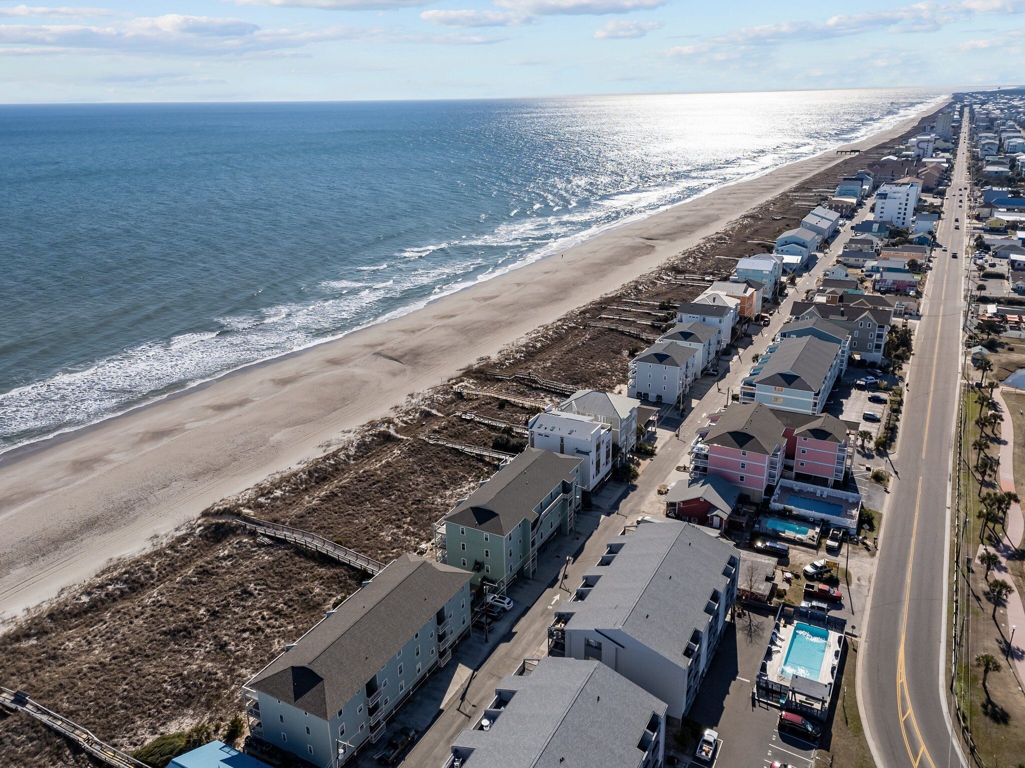 Vista aerea di una zona residenziale costiera con proprietà direttamente sulla spiaggia, una strada e una spiaggia.
