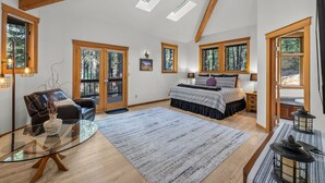 A spacious bedroom with a large bed, a glass coffee table, a leather sofa, and a view of the outdoors through large windows.