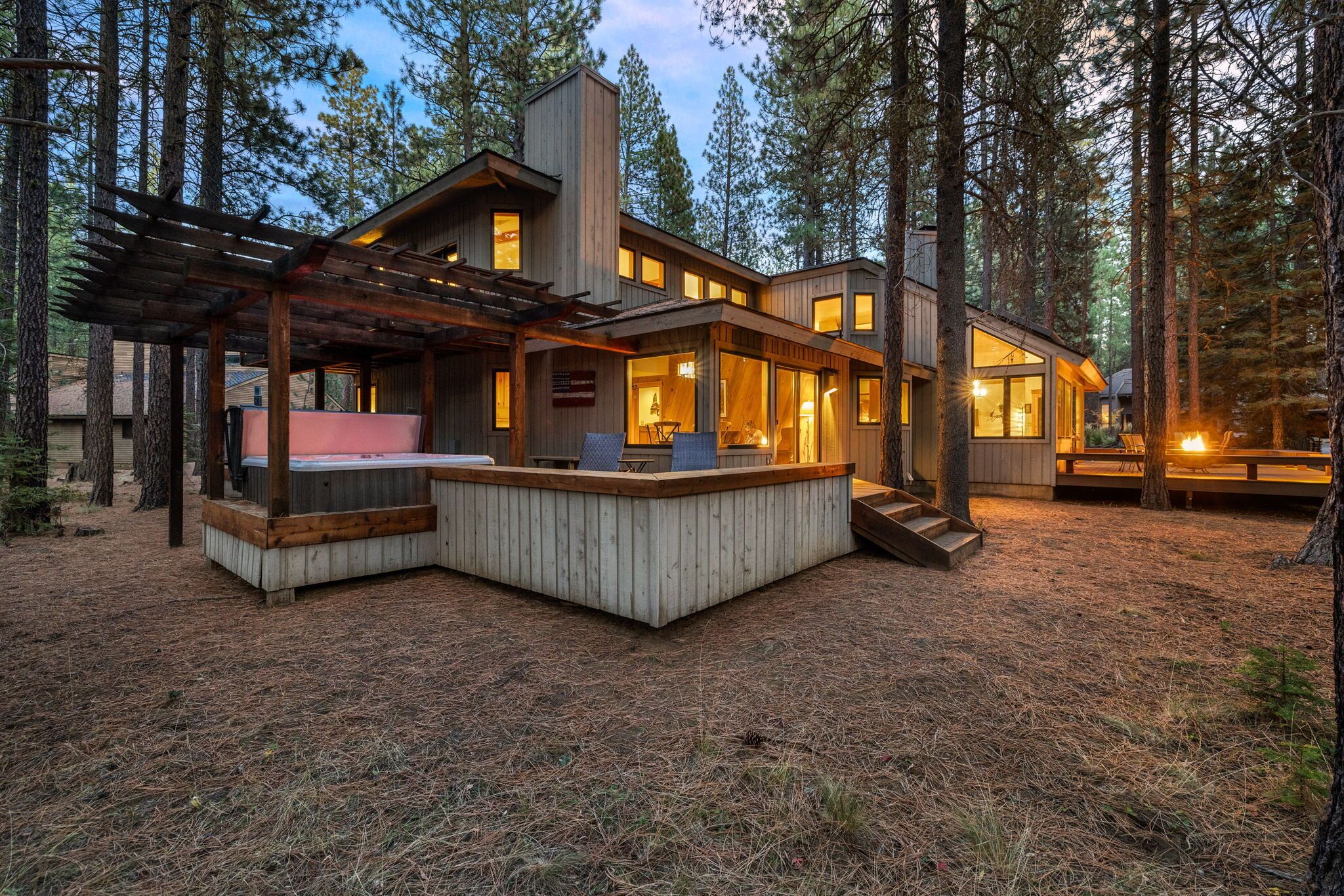 A modern cabin with a hot tub, wooden deck, and large windows.