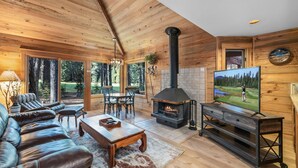 A cozy cabin interior with a fireplace, leather sofa, dining area, and a TV.