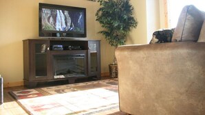 A living room with a flat-screen TV, a dark wooden entertainment center, a large potted plant, and a beige sofa.