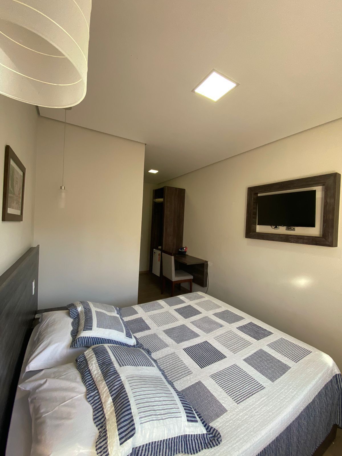 A bedroom with a bed, a TV mounted on the wall, a desk, and a chair.