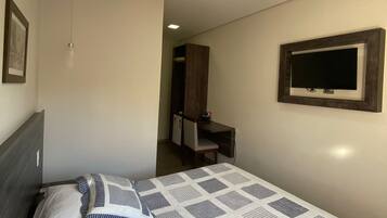A bedroom with a bed, a TV mounted on the wall, a desk, and a chair.