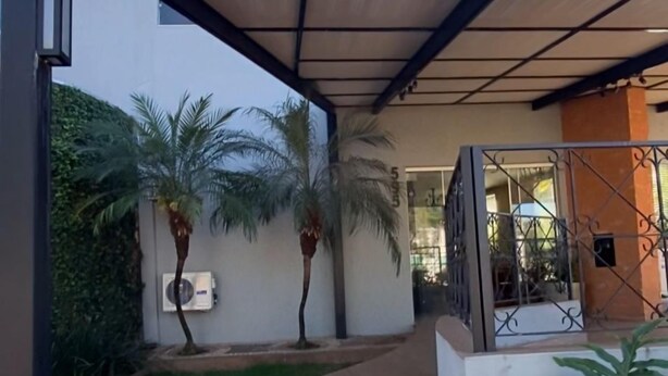 A modern outdoor area with a wooden pathway, palm trees, and a covered seating area. - Hotel Recanto dos Ipês (Frutal)