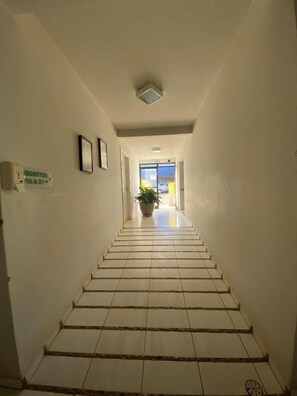 A hallway with a tiled floor leading to a bright area with a plant. - Hotel Recanto dos Ipês (Frutal)