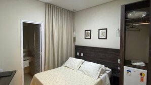 A bedroom with a bed, a desk, a chair, a wardrobe, and a small refrigerator. - Hotel Recanto dos Ipês (Frutal)