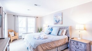 Une chambre à coucher avec un grand lit, une table de chevet avec une lampe, une chaise et une fenêtre avec des rideaux.
