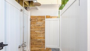 Une salle de bain moderne avec un mur d’accent en pierre, une douche dotée d’un pommeau de douche à pluie et une porte blanche.