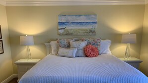 A neatly made bed with a white quilt, two bedside lamps, and a beach-themed painting above it. - Ground floor with King master, 2 twins 2nd bedroom Bunk beds in 3rd bedroom (twins) twin/full combo. (New Smyrna Beach)