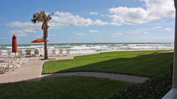 A beachside view with a palm tree, beach chairs, and umbrellas. - Ground floor with King master, 2 twins 2nd bedroom Bunk beds in 3rd bedroom (twins) twin/full combo. (New Smyrna Beach)