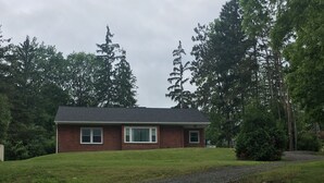 A single-story brick house with a dark roof, surrounded by a gravel driveway and a grassy lawn. - Watkins Glen lake view rental (Watkins Glen)