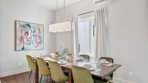 A dining area with a wooden table, green chairs, and a large abstract painting on the wall.