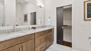 A modern bathroom with a marble vanity, a large mirror, and a dark door leading to a closet.