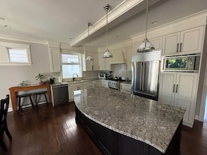 A kitchen with a large island, stainless steel appliances, and pendant lighting.